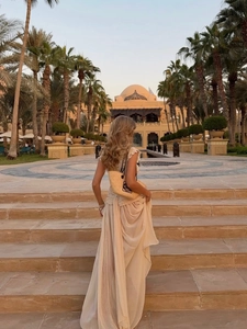 Detail of elegant beige chiffon maxi dress with layered hem and chic straw bag