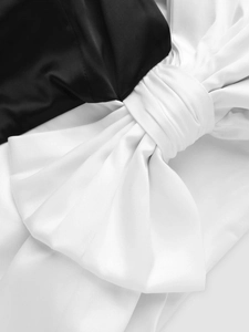 Detailansicht einer großen weißen Satinschleife auf schwarzem Kleid mit feiner Falte