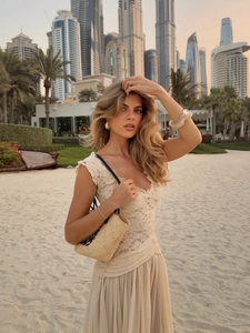 Elegant beige lace and chiffon maxi dress detail with straw handbag at seaside