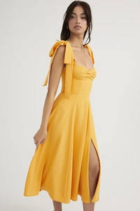 Detail of a bright yellow dress with bow shoulder straps and front leg slit