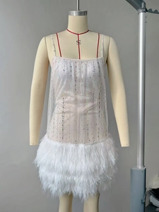 Detail of white party dress showing mesh fabric with sequins and feather trim hem