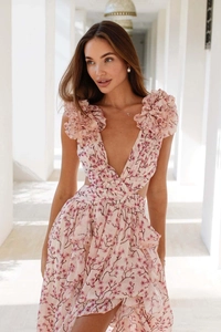 Détail d'une robe fleurie rose clair avec col en V profond, volants et découpe taille