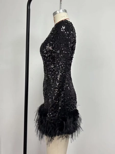 Détail d'une robe noire à paillettes avec manches longues et bordure en plumes sur l'ourlet