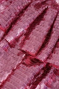 Dettaglio macro del tessuto con paillettes magenta e trama plissettata a rettangoli