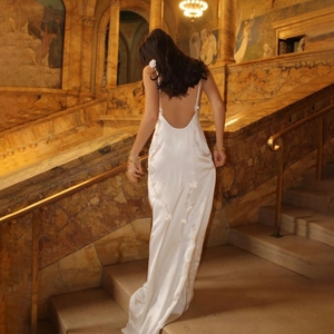 Elegant white satin backless maxi dress with 3D floral details on marble stairs