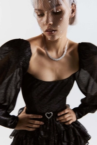 Détail de la robe noire à manches bouffantes avec cœur à la taille et collier brillant