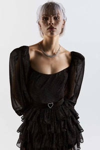 Détail d'une robe en mesh noir avec manches bouffantes et jupe à volants avec ceinture