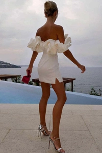 Vue arrière d'une robe moulante blanche à volants et fente latérale au bord de l'eau