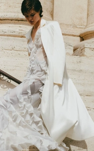Close-up of white layered ruffle dress with a sharp ivory blazer on elegant stone stairs
