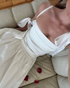 Detail of elegant off-shoulder ivory satin dress with pleated bust and bow straps