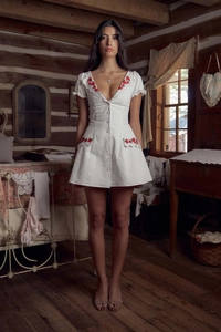 Detail of red rose embroidery and lace trim on a white V-neck cotton linen dress