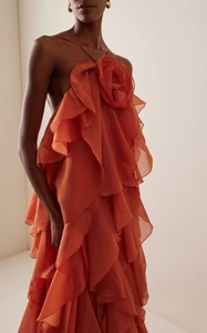 Detailed close-up of 3D floral decoration and tiered ruffles on orange halter maxi dress