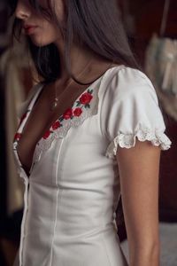 Detail of deep V-neckline with red rose embroidery and white lace trim on a white dress