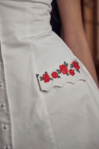 Close-up of white dress featuring delicate red rose embroidery and lace pocket detail