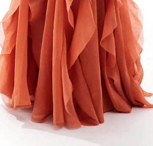 Close-up of rust orange chiffon dress featuring tiered ruffles and wavy hem detail