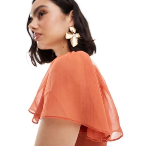 Golden flower earrings with white pearl center on model wearing orange flutter sleeve top