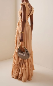 Detail of apricot ruffled evening gown with pleated fabric and a stylish metal ring handbag