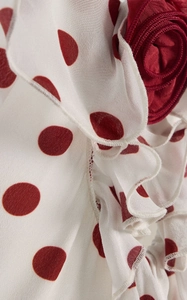 Detailed close-up of red polka dot print fabric with 3D floral accent and ruffle layers