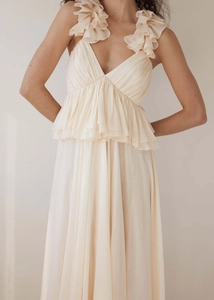 Detailed close-up of cream pleated long dress with decorative ruffle flowers and deep V-neck