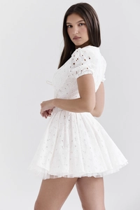 Détail de la broderie blanche ajourée sur robe avec manches bouffantes et ourlet plissé