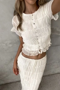 Detail of white chiffon pleated two-piece set featuring ruffled edges and textured fabric