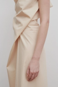 Detail view of beige sleeveless dress showing asymmetric draped fabric and premium texture