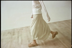 Side view of white long-sleeve top and beige knotted maxi skirt with high drape