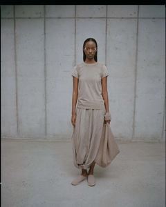 Minimalist beige outfit featuring short-sleeve top and pleated long skirt on neutral wall