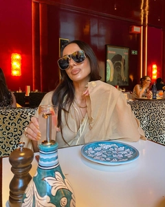 Detail of elegant black aviator sunglasses with gold metal frame and sheer beige tunic dress