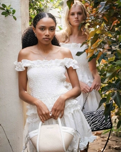 Detail of white off-shoulder smocked dress with intricate embroidery and ruffled edges