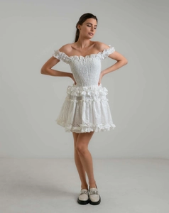 Close-up detail of white smocked dress with intricate embroidery and ruffled cake skirt