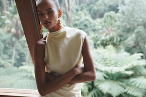 Détail de la robe en satin jaune avec encolure oblique et boucles d'oreilles ambre