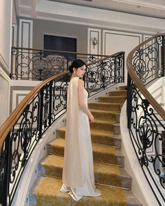 Detail of elegant cream satin evening gown featuring a flowing back cape design on a staircase