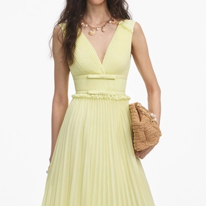 Détail de la robe plissée jaune clair avec des nœuds à la taille et finitions en dentelle