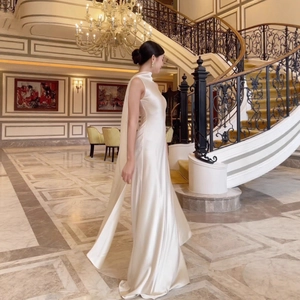 Elegant white satin halter sleeveless evening dress with cape detail in luxury setting