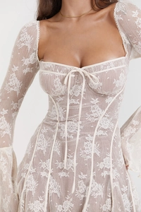 Dettaglio del corpetto in pizzo beige con motivo floreale, fiocco frontale e maniche a campana