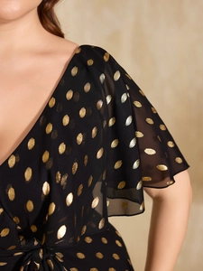 Detail of V-neckline and ruffle sleeves on a black chiffon dress with gold polka dots