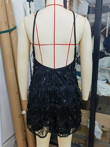 Détail d'une robe courte noire à paillettes avec dos nu et éléments de pompons fins