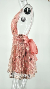 Détail de la robe à paillettes rose corail avec grand nœud en satin et broderie de feuilles d'or