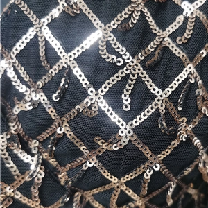 Détail macro de broderies pailletées dorées avec motif losange sur tissu résille noir