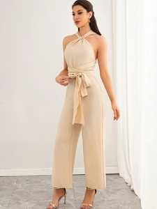 Detail of elegant backless beige jumpsuit with twist neck and belted wide leg trousers