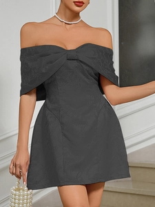 Detail of elegant black off-shoulder mini dress with large bow and floral jacquard texture