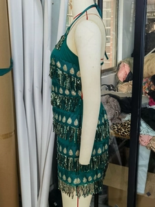 Détail de la robe à paillettes vert émeraude montrant des motifs dorés et de longues franges