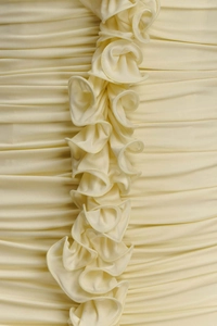 Detailed close-up of cream dress showing ruched fabric texture and vertical ruffles
