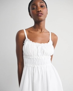 Detailed view of white smocked dress featuring ruffled neckline and thin spaghetti straps
