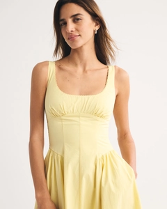 Detail of scalloped trim on neckline and light pleated texture of yellow sleeveless dress