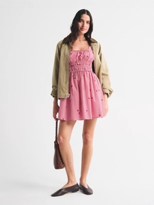 Gingham mini dress with utility jacket and woven handbag on a white background