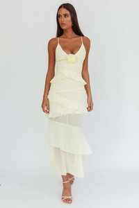 Detail of light yellow ruffle dress featuring a 3D floral accent and tiered hemline