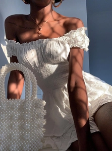 Detail of white off-shoulder mini dress with smocked texture and pearl woven handbag