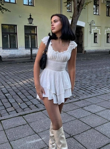 Detail of white cotton mini dress with smocked waist and ruffled hemline textures